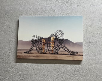 Puede incluir: Una escultura de metal negro de tres figuras, dos de las cuales están de pie dentro de la figura más grande. La escultura está situada en un paisaje desértico.