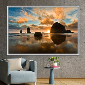 May include: A scenic photograph of a rocky coastline at sunset. The sky is a vibrant mix of orange, pink, and blue with fluffy clouds. The ocean is calm and reflects the colours of the sky. There are several large rocks in the water, including a large, prominent rock in the centre of the image.