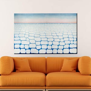 以下が含まれることがあります： 白と青のレンガのようなパターンが特徴的な抽象画で、ピンクと青のグラデーションの空を背景にしています。 このアートワークは、オレンジ色のソファとマッチするクッションの上に展示されており、モダンな美学を作り出しています。