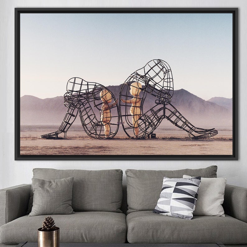 May include: A black metal sculpture of two figures, one larger than the other, standing in a desert landscape. The figures are made of wire mesh and appear to be embracing.
