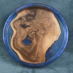 May include: A round wooden tray with a blue resin border. The wood has a natural grain pattern and there is a small blue resin accent in the center.