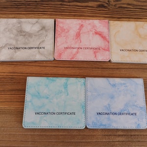 May include: Five different colored card holders with a marble pattern. Each holder has the text "Vaccination Certificate" printed on the front.