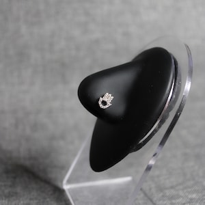 May include: A silver nose ring with a small, clear crystal design in the shape of a hand.