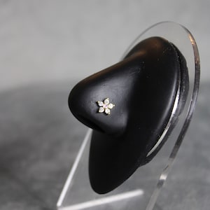 Peut inclure: Un petit anneau de nez en forme de fleur dorée avec des strass transparents.