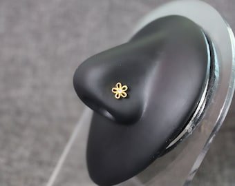 Puede incluir: Un aro de nariz de oro en forma de flor con un solo strass transparente en el centro.