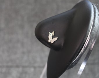 May include: A small, gold butterfly nose ring with clear rhinestones. The ring is displayed on a black stand.