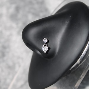 May include: A silver nose ring with a dangling heart-shaped charm and a small clear stone above it.