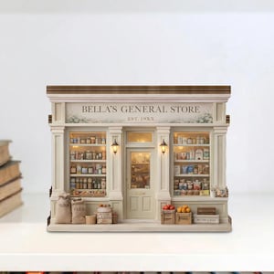 Puede incluir: Una maqueta en miniatura de "Bella's General Store" con una fachada color crema, estanterías detalladas y un techo de madera. La tienda presenta una puerta central, dos ventanas y elementos decorativos como sacos y cajas. El texto "Bella's General Store" se muestra sobre la entrada.