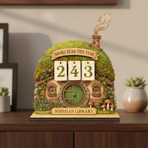 May include: A wooden book counter in the shape of a hobbit house, featuring a green door and mossy roof. The counter shows "243" and the text "BOOKS READ THIS YEAR." The base reads "SOPHIA'S LIBRARY."