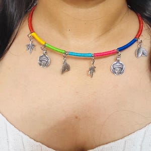 May include: A colorful choker necklace with a rainbow cord. The necklace features silver-toned charms, including leaf and face pendants. The cord is red, yellow, green, blue, and pink.