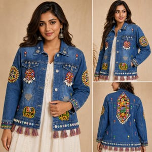 May include: A blue denim jacket featuring colorful embroidered circular and elephant motifs, silver-toned metal charms, and white cowrie shells. The hem is finished with a row of multicolored fabric tassels, and the back displays a large central embroidered panel.