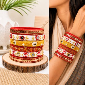Könnte beinhalten: Ein Stapel aus sechs Armreifen mit verschiedenen Designs, darunter roter Faden mit goldenen Pailletten, weißer Faden mit Spiegeln und gelber Stickerei, gelber Faden mit Perlen, roter Faden mit goldenen geometrischen Mustern und weißer Faden mit Spiegeln.
