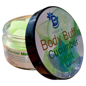 Puede incluir: Un tarro transparente de exfoliante corporal de pepino y menta con tapa negra. La tapa presenta el texto "Body Buff Cucumber Mint" sobre un fondo de rodajas de pepino. El tarro contiene cubos verdes de exfoliante corporal.