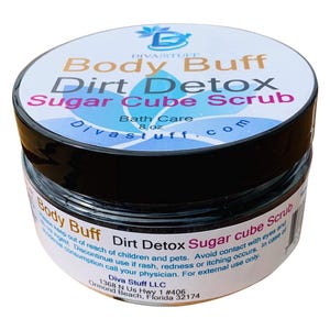 Puede incluir: Un tarro de exfoliante de azúcar Body Buff Dirt Detox de Diva Stuff. La etiqueta presenta el nombre del producto en varios colores, con "Bath Care" y "8 oz" también mostrados. El tarro tiene una tapa negra y un cuerpo transparente.