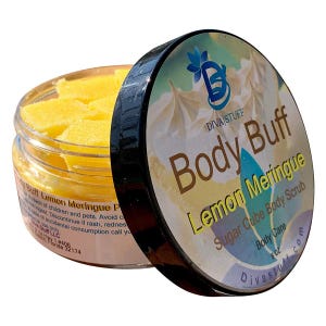 Puede incluir: Un tarro de exfoliante corporal Diva Stuff Body Buff Lemon Meringue Sugar Cube. El tarro está abierto, revelando cubos de azúcar amarillos. La tapa, con borde negro, muestra el nombre y el logotipo del producto. El producto es 227g.