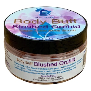Puede incluir: Un tarro de exfoliante corporal de azúcar Body Buff Blushed Orchid de Diva Stuff. El tarro tiene una tapa negra y una etiqueta con el nombre del producto y un diseño floral. La etiqueta también incluye el peso del producto, 227g.