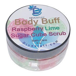 Puede incluir: Un tarro transparente de exfoliante corporal con tapa negra. La etiqueta dice "Body Buff Raspberry Lime Sugar Cube Scrub" con una ilustración de frambuesa y lima. El tarro contiene cubos de azúcar rosas y verdes. El producto es de 227 g.