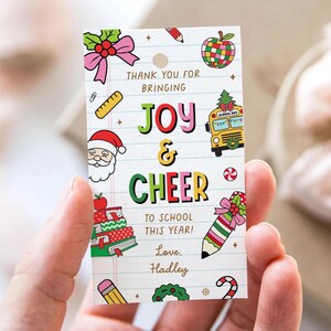 May include: A rectangular gift tag with a hole at the top, featuring the words "THANK YOU FOR BRINGING JOY & CHEER TO SCHOOL THIS YEAR!" and "Love, Hadley." The tag includes illustrations of a school bus, Santa, and other school-themed graphics.