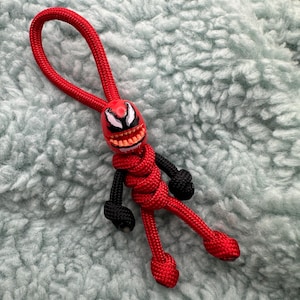 Può includere: Portachiavi in paracord rosso e nero con un ciondolo a forma di personaggio Venom. Il portachiavi è legato a forma di figura con paracord nero e rosso.