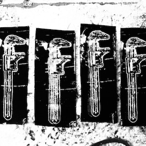May include: A monochrome image showing four prints of a caliper tool on a textured surface. The prints are rectangular and arranged in a row. A pair of scissors is in the foreground. The image has a distressed, grunge style.