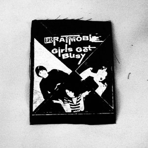 Peut inclure: Patch noir et blanc avec le texte "Bratmobile Girls Get Busy" et un graphique de deux personnes.