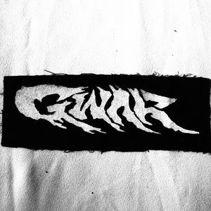 May include: Black and white embroidered patch with the word "GENRE" in a stylized font.