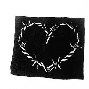 Puede incluir: Parche de tela negro con un diseño de corazón de alambre de púas blanco.