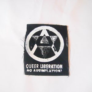 May include: Black and white patch with a stylized anarchy symbol and the text "Queer Liberation No Assimilation?"