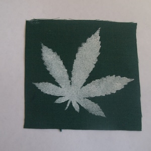 May include: A dark green fabric patch with a white marijuana leaf design.