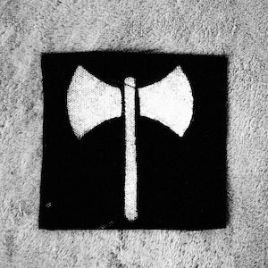 Könnte beinhalten: Ein Schwarzweißbild eines feministischen Symbols, einer Doppel-Axt, die auf eine strukturierte Oberfläche gemalt ist.