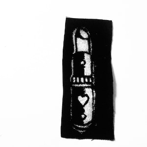 May include: Black fabric patch with a white design of a keyhole with a heart inside. The keyhole is surrounded by a decorative border.