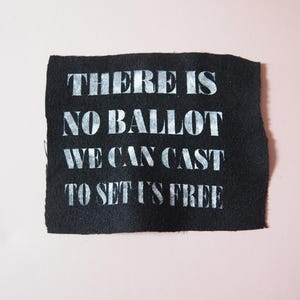 May include: Black fabric patch with white text that reads "There is no ballot we can cast to set us free".
