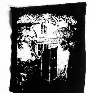 May include: Black and white patch with a graphic of two people wearing gas masks in front of a building with the word "Desolation" above them.