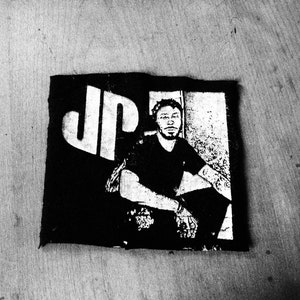 May include: Black and white image of a person with the letters "JP" in the background.