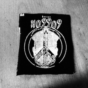 Peut inclure: Patch noir avec un symbole de paix blanc et le texte "HO9909" en blanc.
