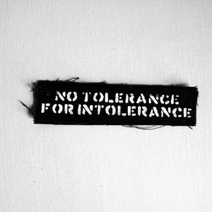 Könnte beinhalten: Schwarz-weißes Patch mit dem Text "NO TOLERANCE FOR INTOLERANCE" in weißen Buchstaben.
