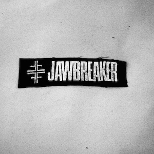 Könnte beinhalten: Schwarz-weiß gestickter Patch mit dem Text "#JAWBREAKER" in weißen Buchstaben.
