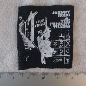 May include: Black and white embroidered patch with the text "Johnny Hobo and the Freight Trains" and the words "Cheap Whiskey" in a smaller font. The patch features a graphic of a train.