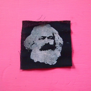 Könnte beinhalten: Schwarzer Stoff-Patch mit einem weißen und grauen Bild von Karl Marx' Gesicht.