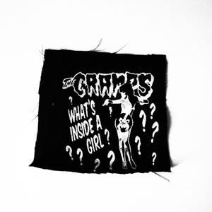 Peut inclure: Patch noir et blanc avec le texte "The Cramps" et "What's Inside A Girl?" avec des points d'interrogation autour du texte. Une image stylisée d'une femme est au centre du patch.