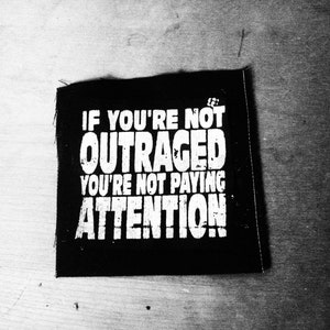 May include: Black and white patch with the text "If you're not outraged you're not paying attention!"