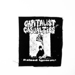 May include: Black and white patch with the text "Capitalist Casualties" and "Raised Ignorant" in a punk rock style.