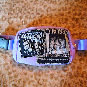 Puede incluir: Una riñonera lavanda con parches negros cosidos. Los parches tienen texto blanco que dice "GRAVES", "WHAT'S INSIDE A GIRL?" y "WITCH FEVER".