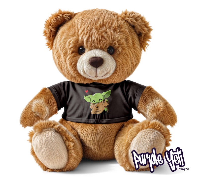 Op de afbeelding: Een bruine teddybeer met een zwart t-shirt met een groene cartoonfiguur. De beer heeft een zacht, pluche uiterlijk en zit rechtop. De afbeelding bevat de tekst "Purple Yeti Trading Co."