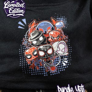 May include: Black t-shirt featuring a graphic of various Spider-Man characters in a cartoon style. The design includes Spider-Man, Spider-Gwen, Spider-Ham, and others. The shirt has the text "Limited Edition" and "Purple Yeti Trading Co."