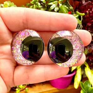 以下が含まれることがあります： ピンクのグリッターの縁取りが施された、丸い黒いプラスチック製の目2つ。目の直径は約2.5cmです。