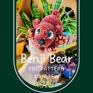 May include: A handmade, red crocheted bear with large, expressive eyes and a black nose. The bear is labeled "Benji Bear" with "PDF PATTERN LOW SEW" text. The bear is surrounded by green plants.