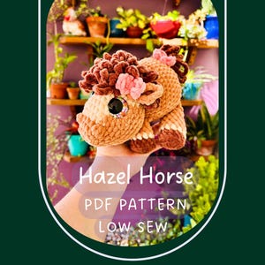 May include: A crocheted horse toy in shades of brown, tan, and cream, adorned with pink flowers. The text "Hazel Horse PDF Pattern Low Sew" is displayed below the horse. The toy has large, expressive eyes.