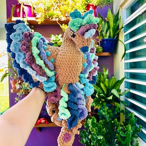 May include: A handmade, plush bird in shades of brown, blue, teal, and purple. The bird has a detailed, textured design with a long neck and a fan-shaped tail. The wings are made of layered, colorful yarn.