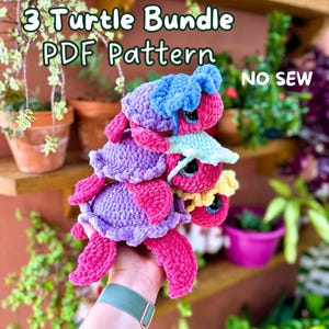 May include: A set of three crocheted turtle amigurumi patterns. The turtles are stacked on top of each other and are made in shades of pink, purple, blue, and yellow. The pattern is a PDF download and is a no-sew project.